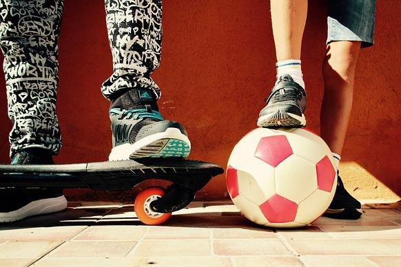 Zwei Beine von Jungen mit Skateboard und Ball
